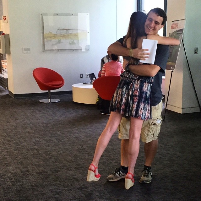 Woman (Lauren, project creator) hugging man (best friend with Lyme disease), holding a note and smiling.